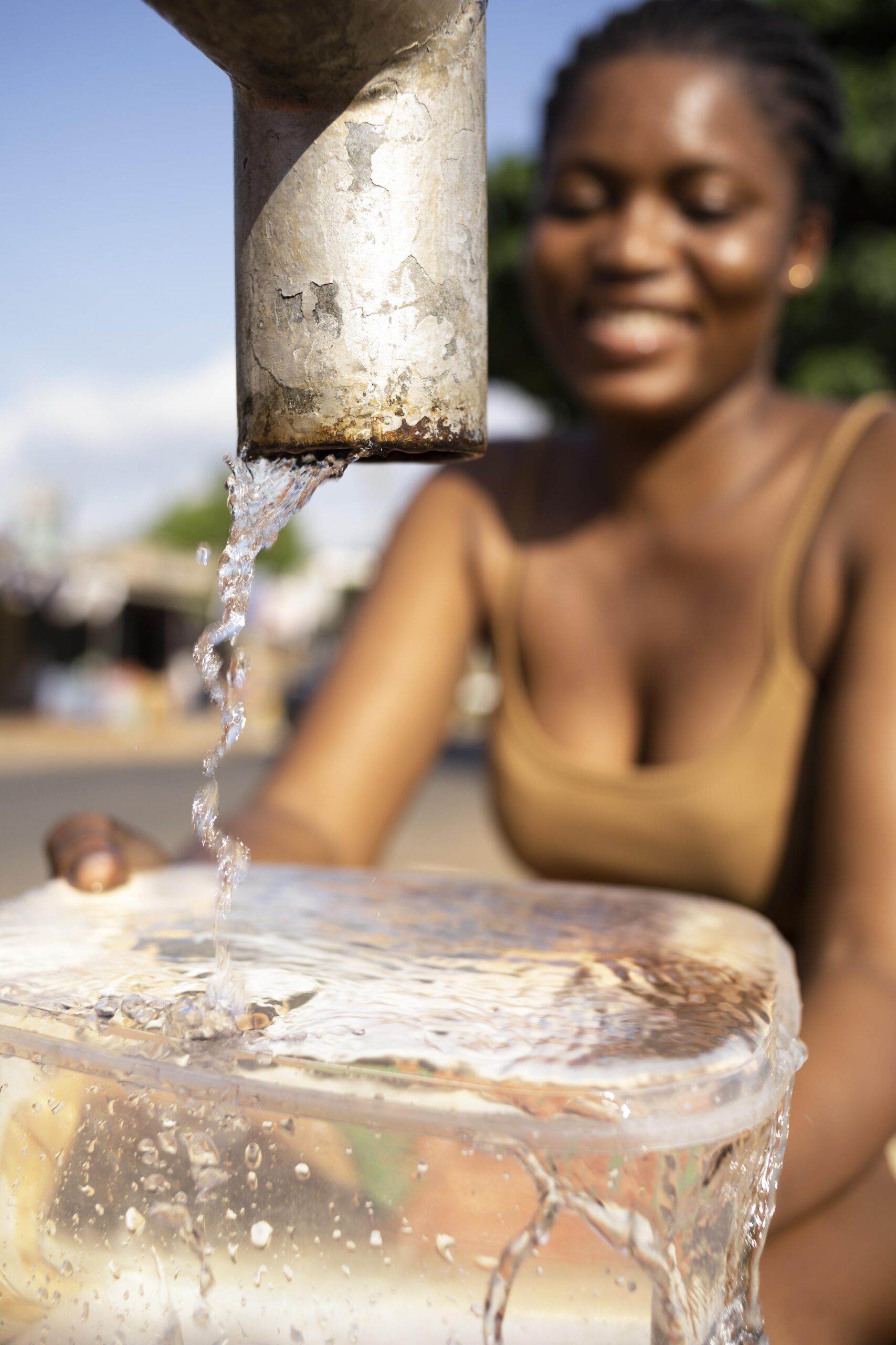 Mulher pegando água limpa da torneira em recipiente, simbolizando uso consciente e sustentável da água