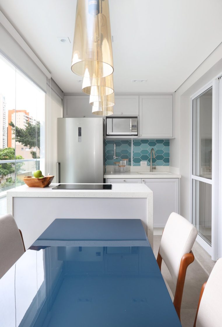 Cozinha funcional e bonita com iluminação natural, mesa azul e armários brancos em espaço compacto